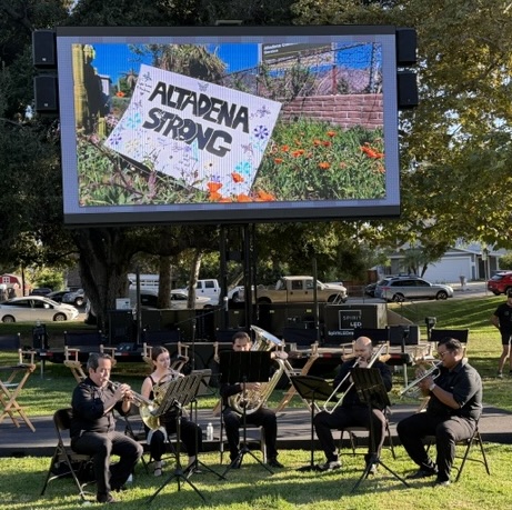 a projector screen showing a sign saying Altadena Strong above a brass band on a stage