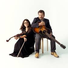 a woman holding a violin seated at the feet of a man holding a guitar